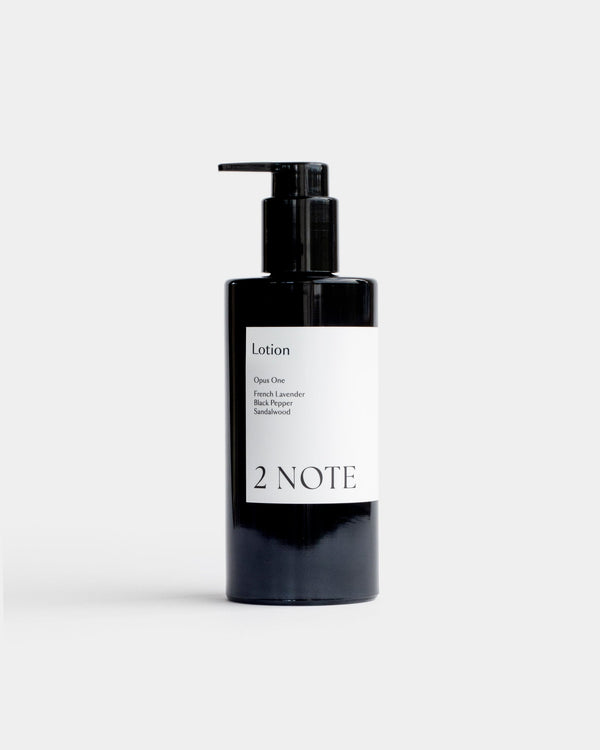 Lotion in tall matte black pump bottle — botanical skincare body lotion with French Lavender, Black Pepper, and Sandalwood, front view on light gray