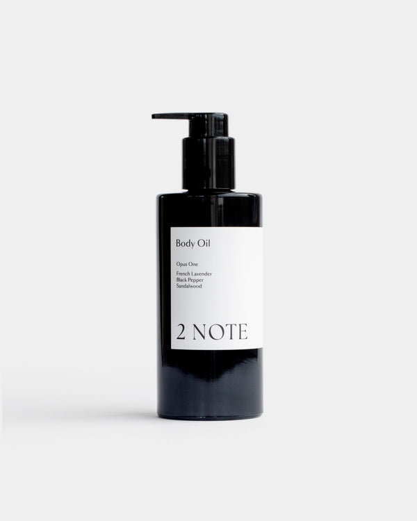 Body Oil in tall matte black pump bottle — botanical skincare dry body oil with French Lavender, Black Pepper, and Sandalwood, front view on light gray