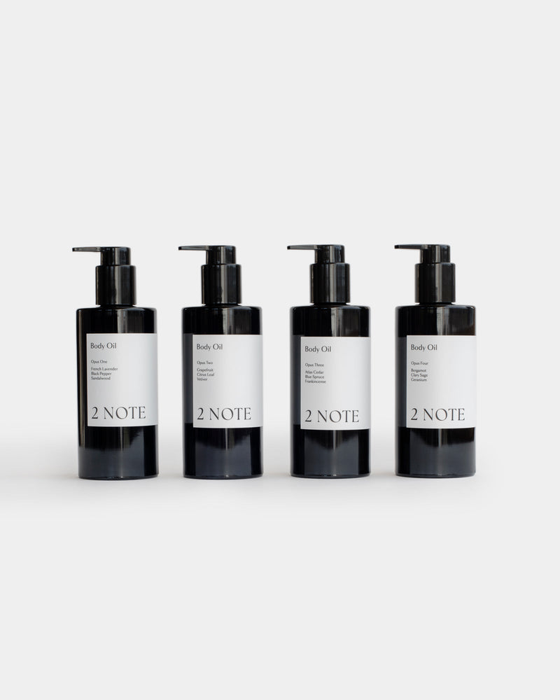 Four Body Oil matte black pump bottles side by side — all scent variants of this botanical skincare dry body oil, light gray background