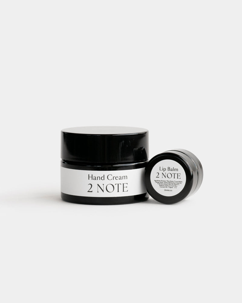 The Nourishing Set — Hand Cream matte black glass jar and Lip Balm small matte black jar side by side on light gray, botanical natural skincare hand and lip care duo