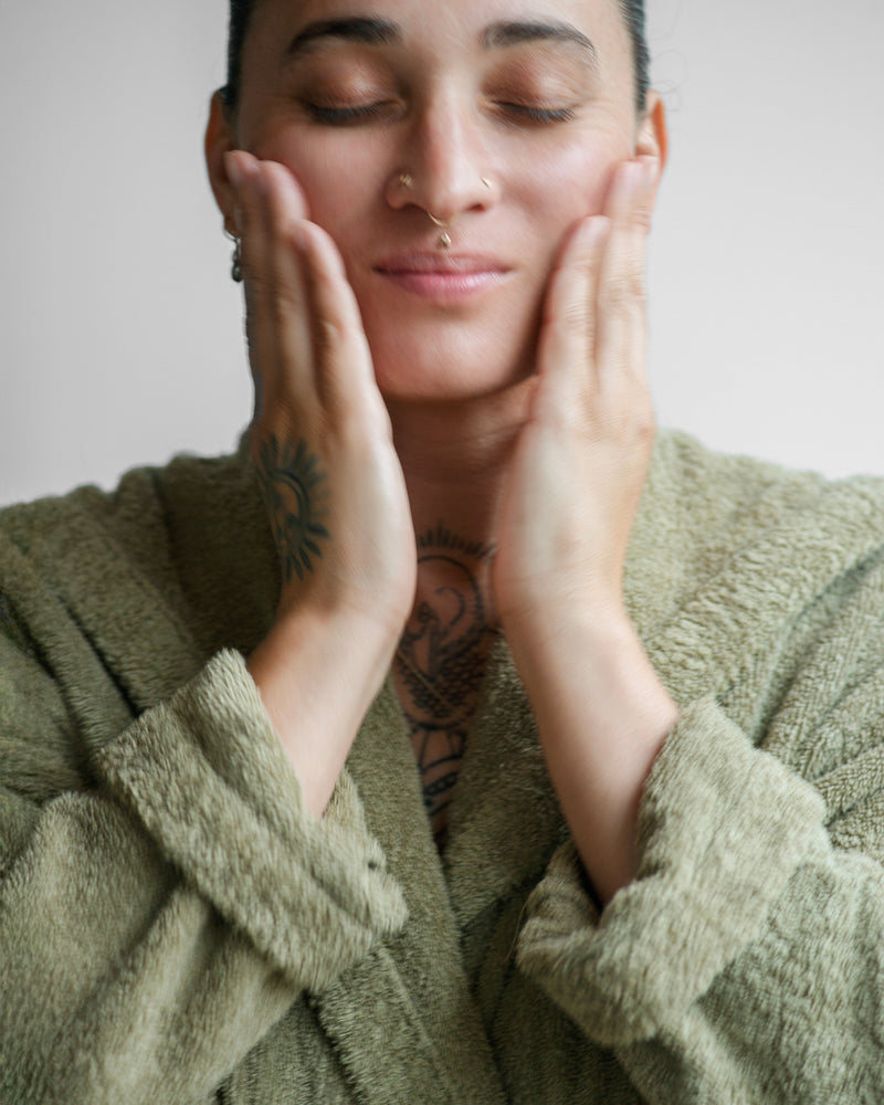 Queer nonbinary model with light olive complexion applying Nourishing Face Oil — natural botanical skincare, close-up