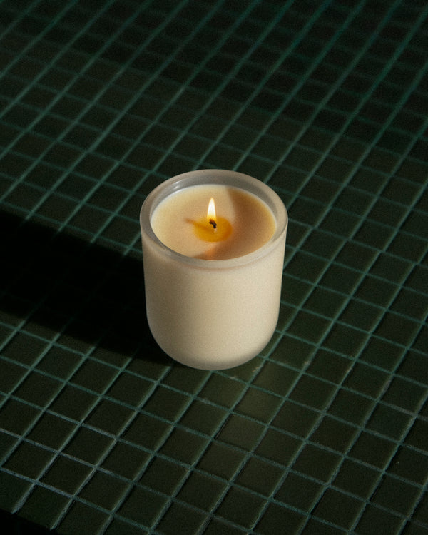 Aromatic Candle lit in frosted white glass vessel on dark green glazed tile — botanical fragrance candle glowing in moody low light