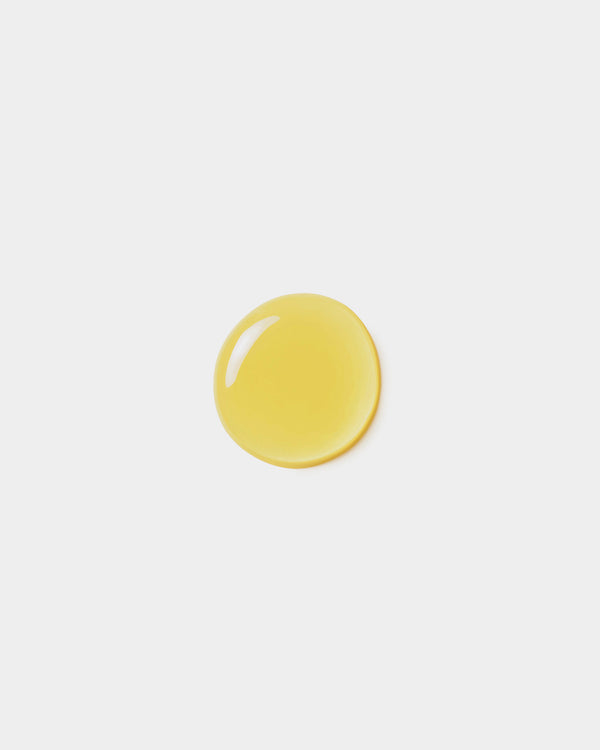 Body Oil formula swatch — single golden yellow botanical oil drop on light gray surface, natural skincare dry body oil texture