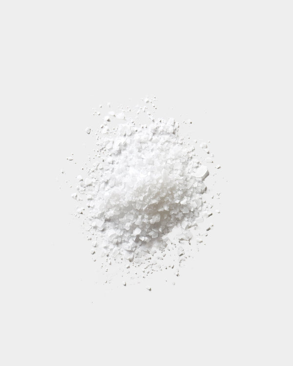Salt Soak formula texture — coarse white mineral salt crystals on light gray surface, botanical skincare bath ingredient
