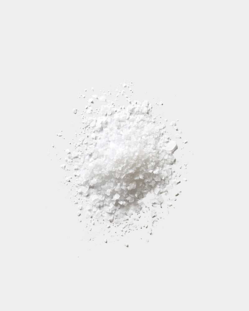 Salt Soak formula texture — coarse white mineral salt crystals on light gray surface, botanical skincare bath ingredient