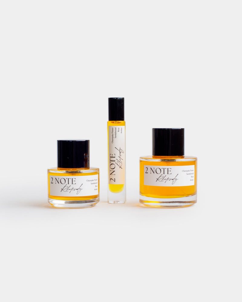 Rhapsody botanical fragrance in three sizes — small and large spray bottles and a roller, warm amber oil through clear glass