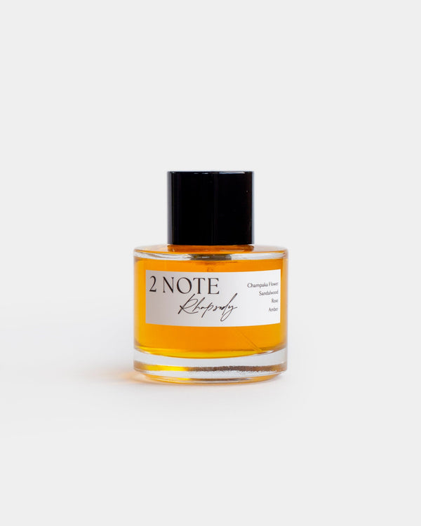 Rhapsody in clear glass spray bottle — botanical natural fragrance, warm orange-amber oil, front view on white