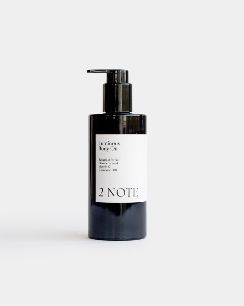 Luminous Body Oil in tall matte black pump bottle — botanical skincare brightening body oil with Bakuchiol, Strawberry Seed, Vitamin C, and Coenzyme Q10, front view on light gray