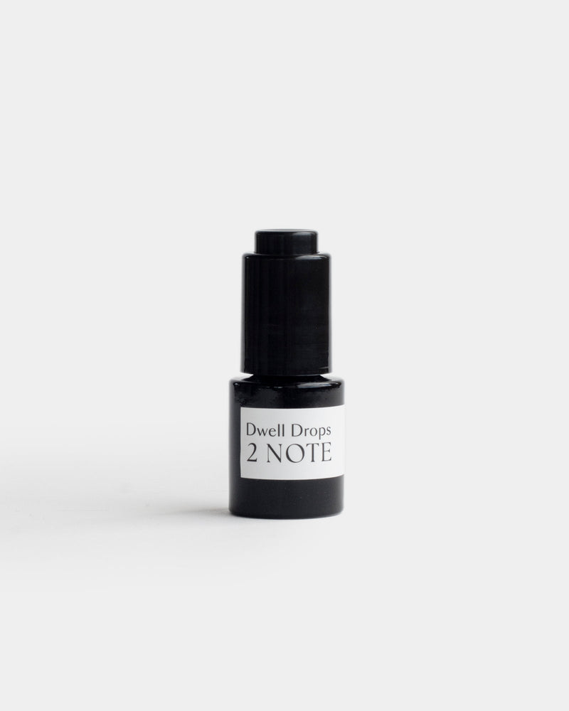 Dwell Drops in small matte black glass dropper bottle — botanical fragrance room drops for natural home fragrance, front view on light gray