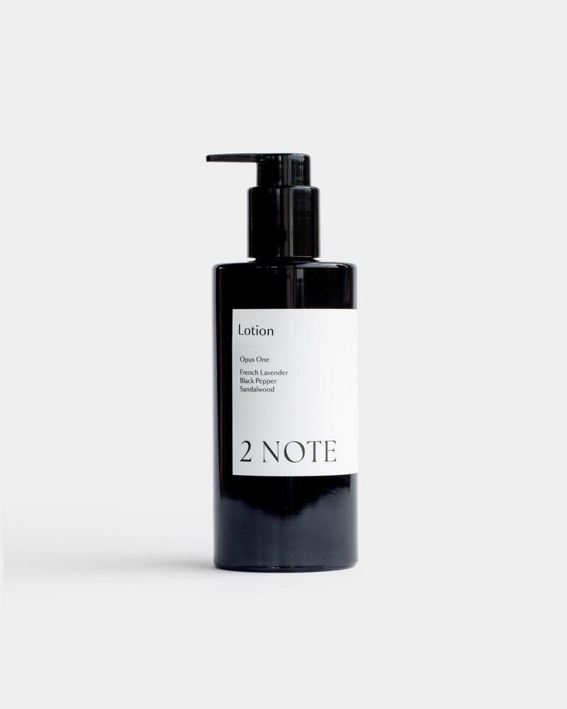 Lotion in tall matte black pump bottle — botanical skincare body lotion with French Lavender, Black Pepper, and Sandalwood, front view on light gray