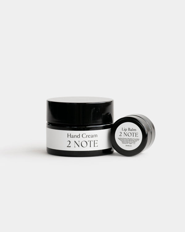The Nourishing Set — Hand Cream matte black glass jar and Lip Balm small matte black jar side by side on light gray, botanical natural skincare hand and lip care duo