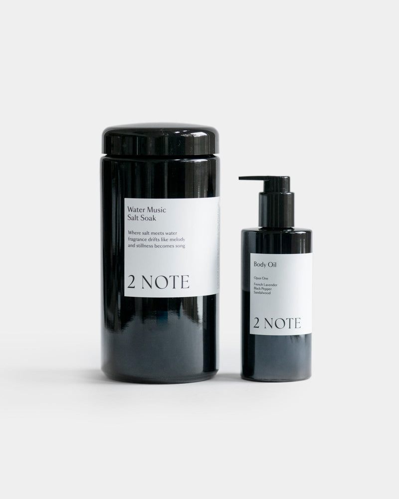 The Renewal Set — Water Music Salt Soak matte black cylindrical jar and Body Oil pump bottle side by side on light gray, botanical skincare bath and body ritual