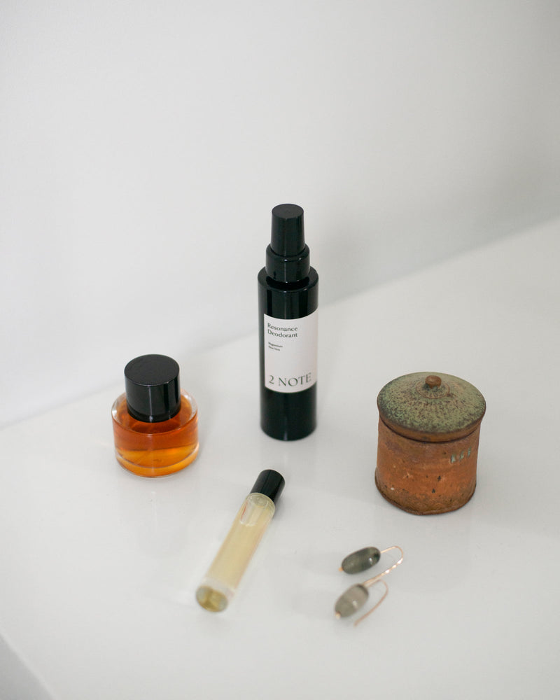 Resonance Deodorant with amber glass bottle, roller, crystal earrings, and ceramic jar — botanical skincare deodorant in a curated shelf vignette