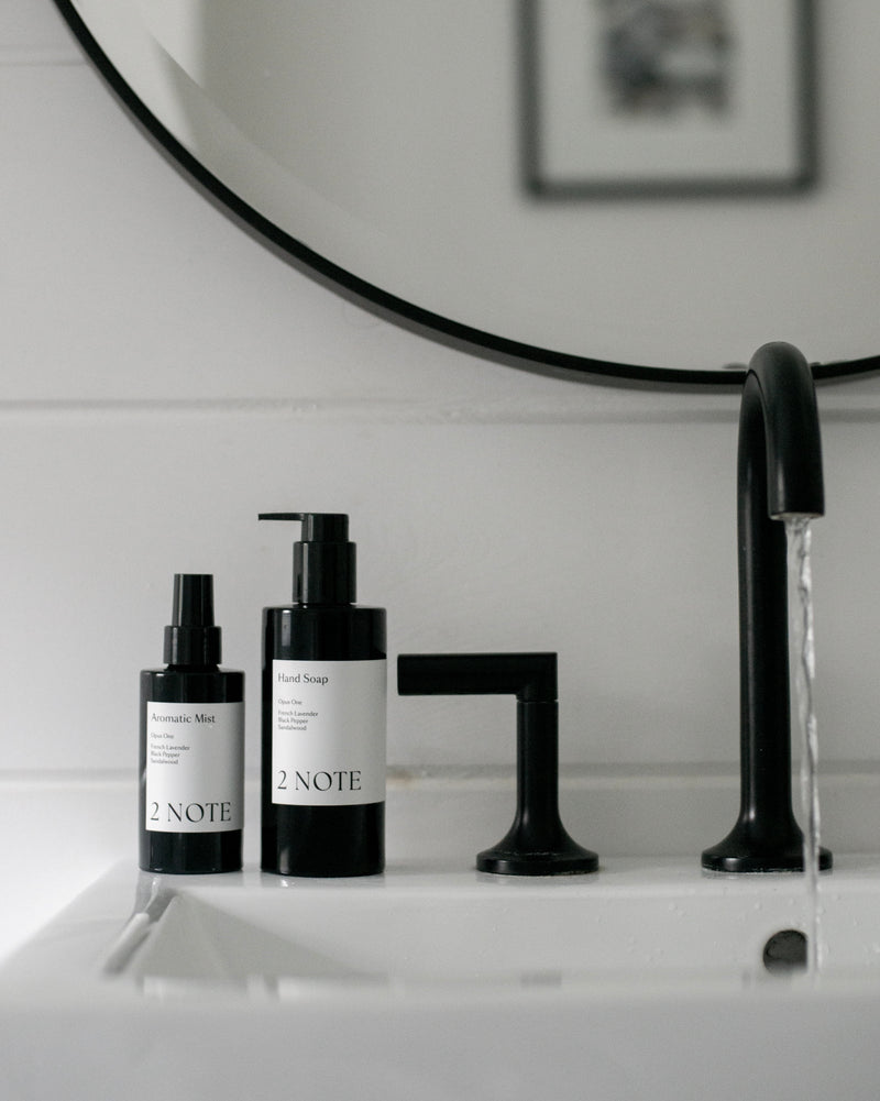 Aromatic Mist and Hand Soap on white porcelain sink counter beside modern matte black faucet — botanical fragrance and natural skincare bathroom vanity pairing