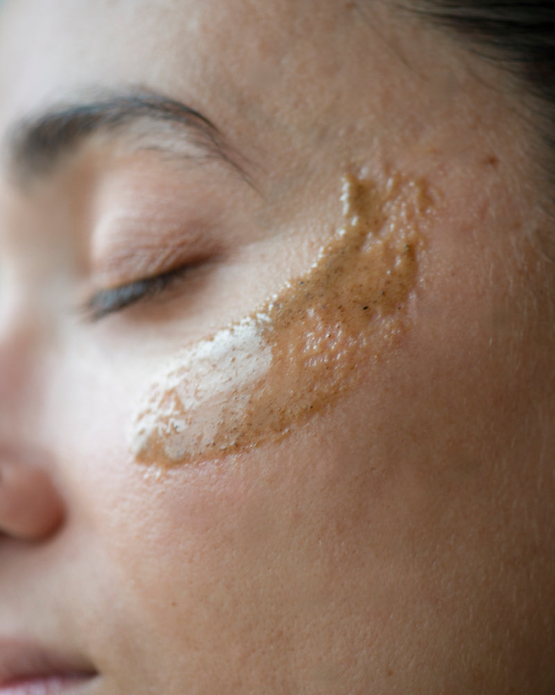 Queer nonbinary model with light olive complexion applying Honey Face Scrub — natural botanical skincare exfoliator, close-up