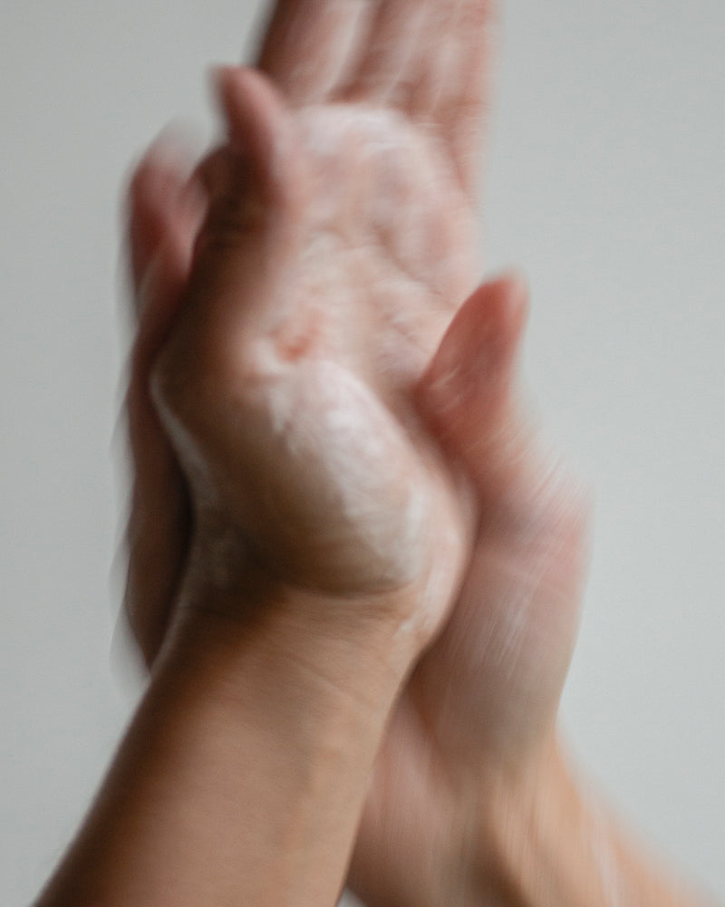 Hands of queer nonbinary model with light olive complexion lathering with Hand Soap foam — botanical skincare hand wash in use, close-up with motion blur on soft gray
