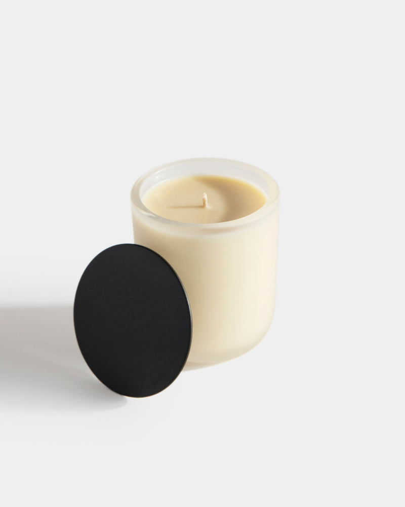 Aromatic Candle frosted white vessel open, black lid leaning beside it — botanical fragrance candle showing cream wax and unlit wick, light gray
