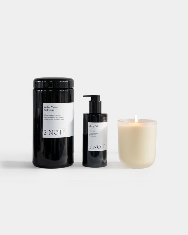 The Bath Set — Water Music Salt Soak, Body Oil, and lit Aromatic Candle side by side on light gray, botanical skincare and botanical fragrance bath ritual trio