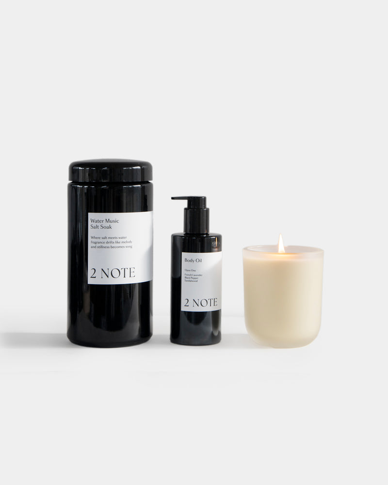 The Bath Set — Water Music Salt Soak, Body Oil, and lit Aromatic Candle side by side on light gray, botanical skincare and botanical fragrance bath ritual trio