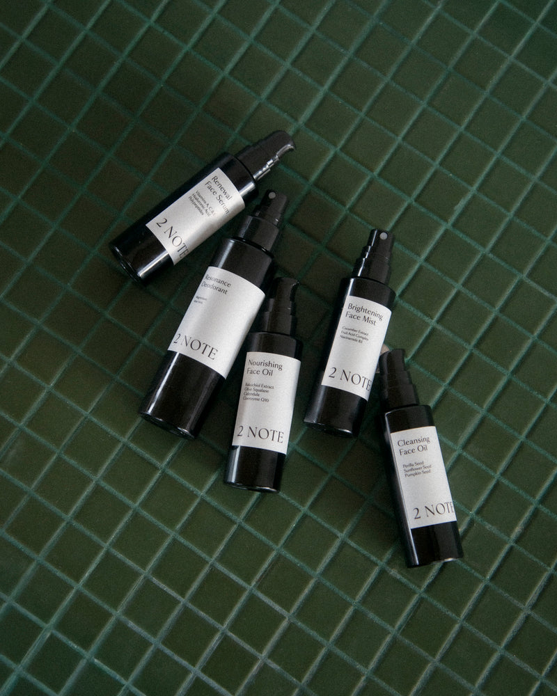 Five 2 Note botanical skincare bottles fanned out on dark green tile — Cleansing Face Oil shown with the full natural skincare collection