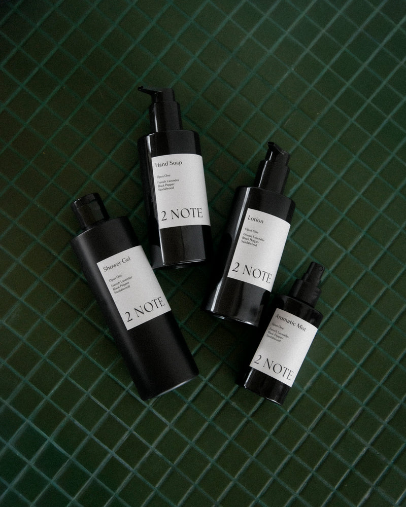 The Quartet Gift Set — Shower Gel, Hand Soap, Lotion, and Aromatic Mist matte black bottles scattered on dark green glazed tile, botanical skincare botanical fragrance flat-lay