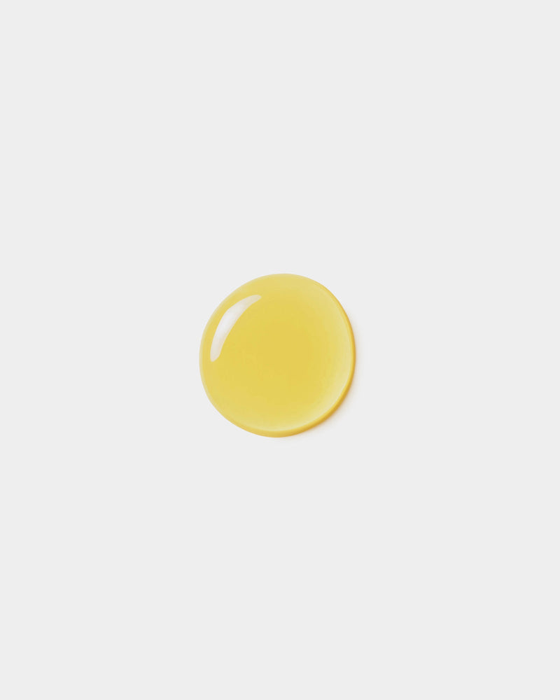 Body Oil formula swatch — single golden yellow botanical oil drop on light gray surface, natural skincare texture