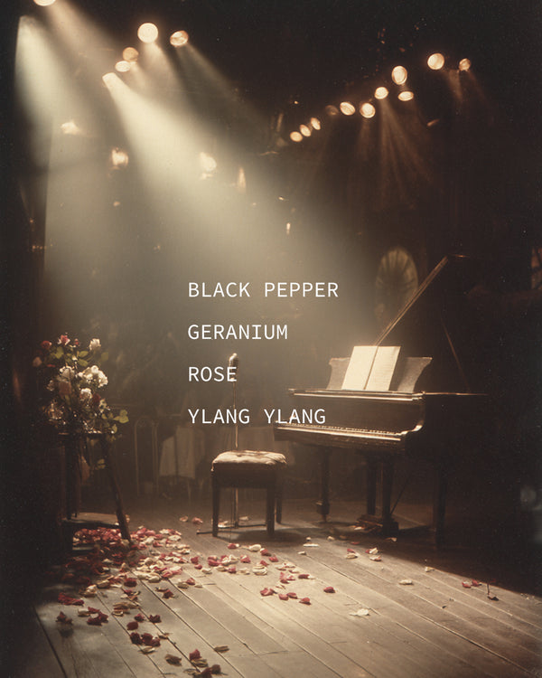 Grand piano on a spotlit stage with rose petals on the floor — mood portrait for Encore botanical fragrance with Black Pepper, Geranium, Rose, and Ylang Ylang