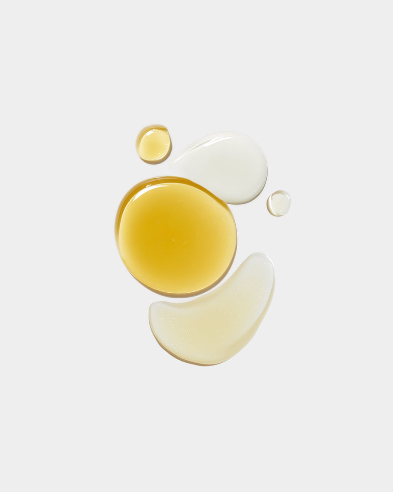 Face Ritual Set formula swatches — golden yellow oil drop, two white cream smears, and small oil drop arranged on light gray, botanical natural skincare textures