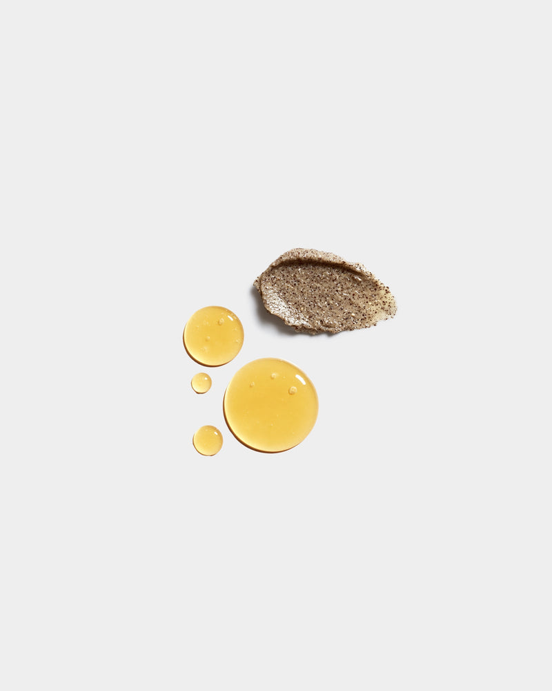 Honey Set formula swatches — golden amber liquid drops and sandy textured scrub swatch on light gray, botanical natural skincare cleansing ingredients