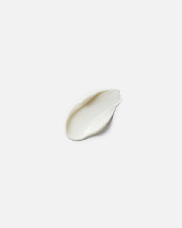 Lotion formula swatch — single off-white cream drop on light gray surface, botanical natural skincare texture