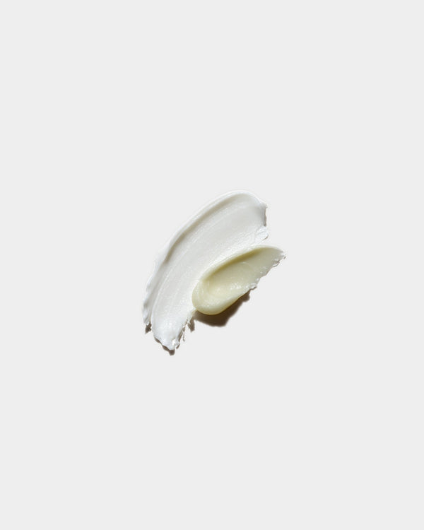 Nourishing Set formula swatch — off-white botanical skincare cream smear with golden oil center on light gray surface